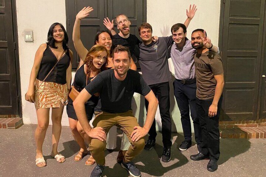 A group of people posing in front of a building with dark doors. 1