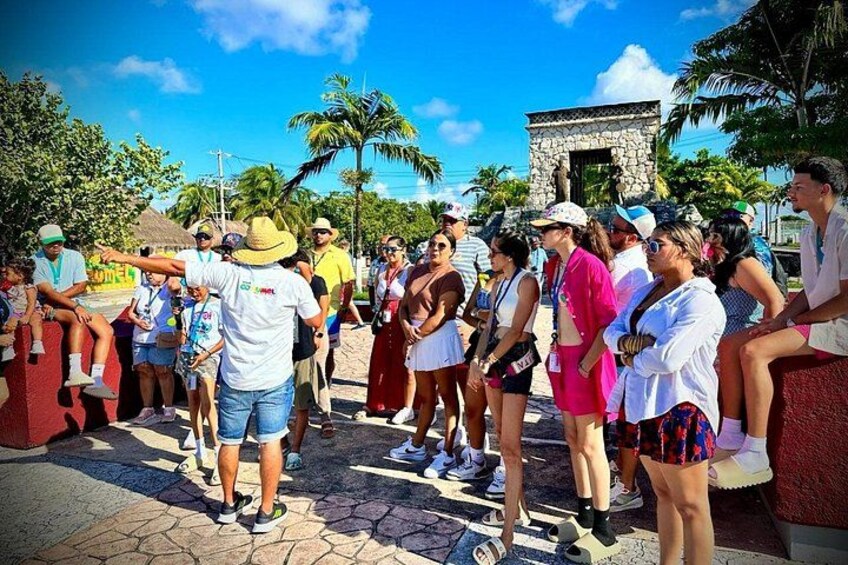 A group of people standing outdoors, some wearing hats and sunglasses, with palm trees and a stone structure in the background. 5