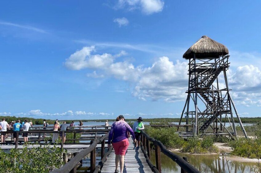 A wooden boardwalk leading to a thatched-roof lookout tower by a body of water. 1