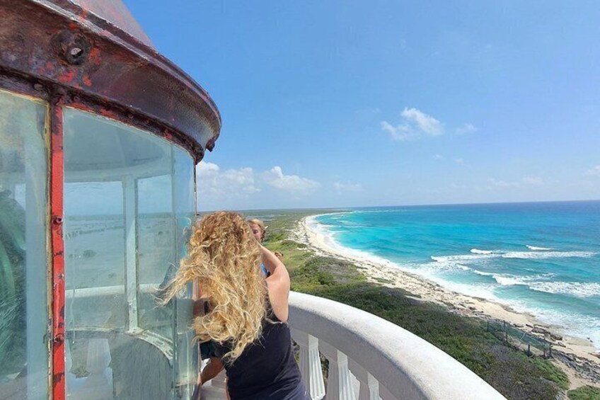 A person with blonde hair standing by a window overlooking a beach with turquoise waters. 5