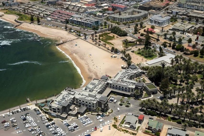 An aerial view of a coastal city with a beach, a parking lot, and a mix of residential and commercial buildings. 3