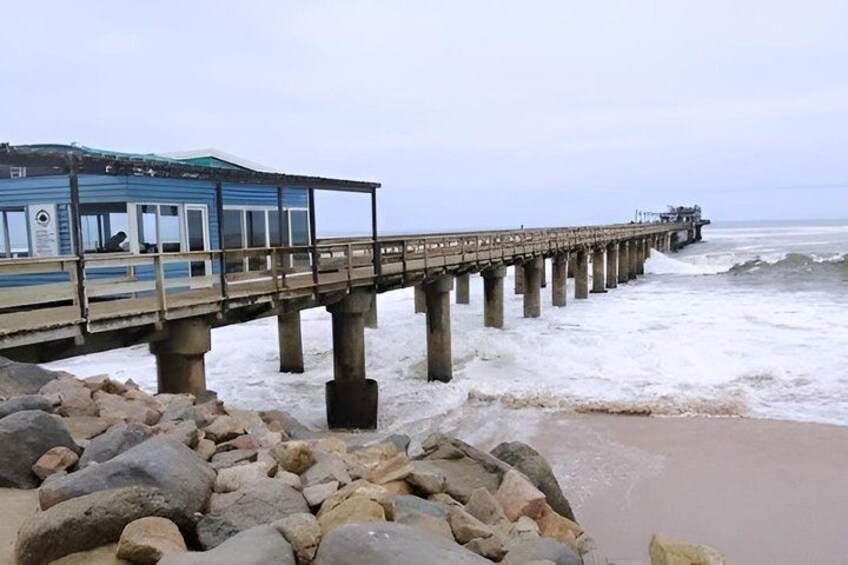 A pier extending into the sea with a building at the end, surrounded by rocks and waves. 2
