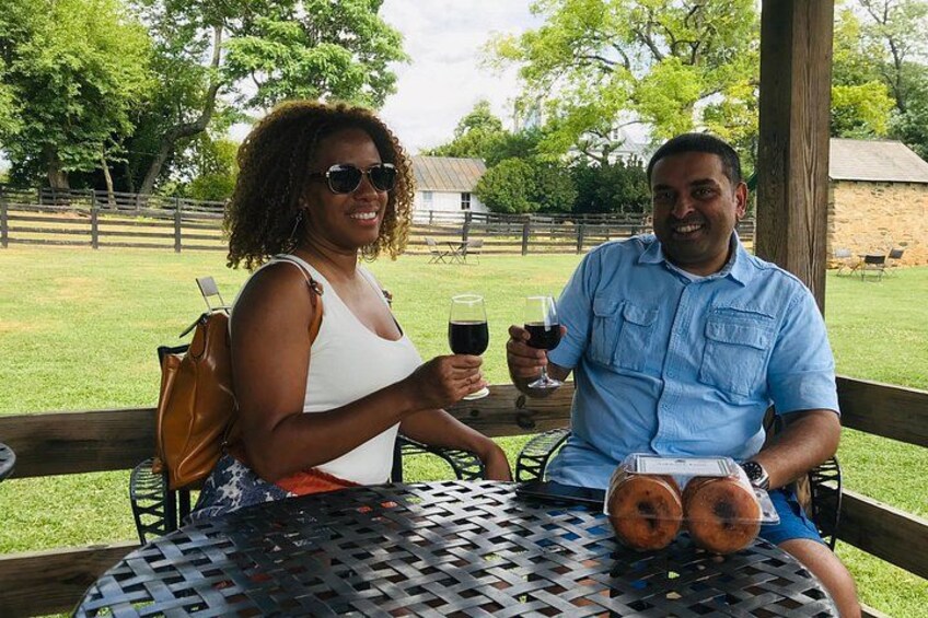 Two people sitting at a table outdoors with drinks and a loaf of bread. 3