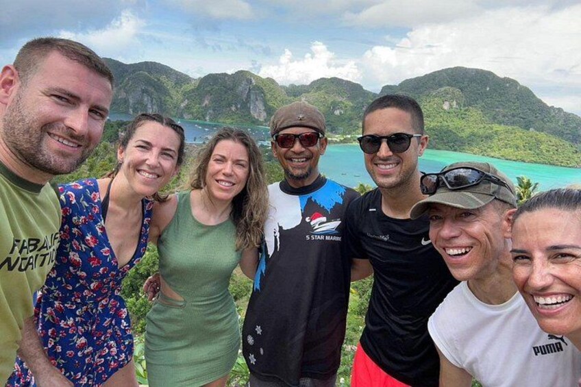 A group of people standing by a scenic coastal landscape with mountains and a body of water. 2