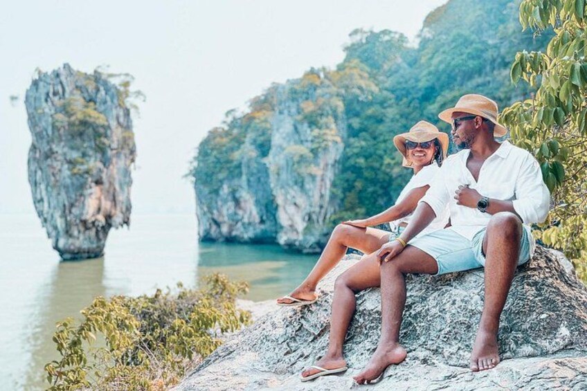 Two people sitting on a rock by a body of water with large rock formations in the background. 4
