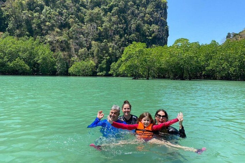 A group of people floating in clear turquoise water with a forested cliff in the background. 3