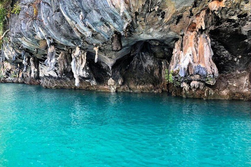 A cave with stalactites and stalagmites, turquoise water, and rocky formations. 2