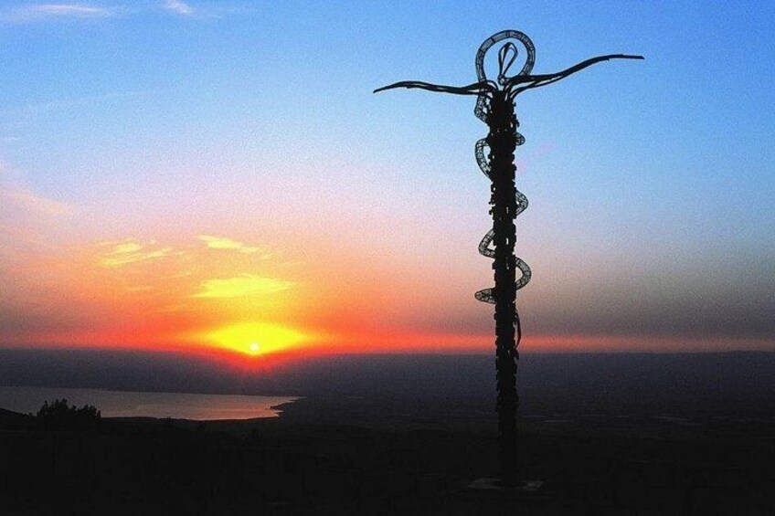 A sculpture of a snake with a circular head and curved tail, set against a sunset over a body of water and distant landscape. 1