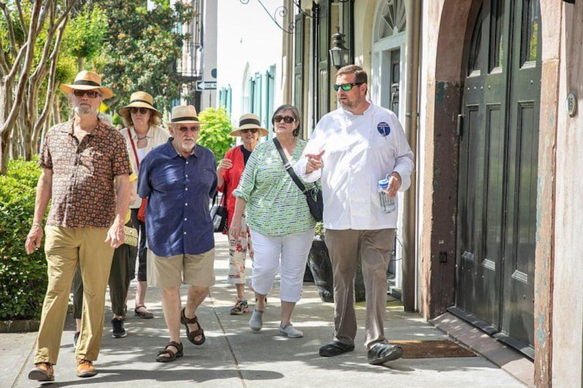 Un grupo de personas caminando por una acera en una zona urbana con edificios y vegetación. 5