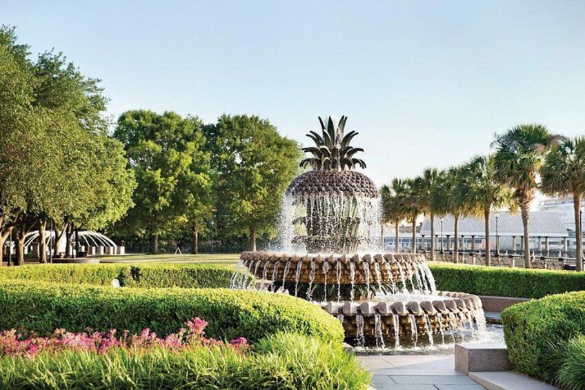 A tiered water fountain surrounded by manicured hedges and palm trees. 1