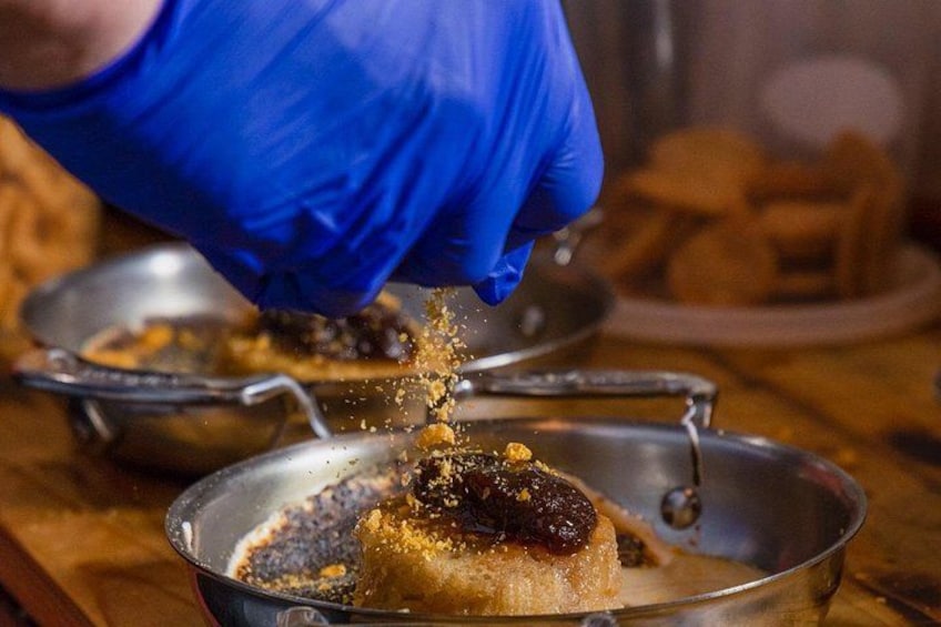 A person wearing blue gloves seasoning a dish in a pan. 5