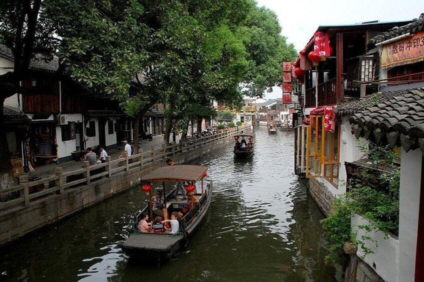 A narrow waterway with traditional buildings on either side, a boat with passengers, and a bridge in the background. 5