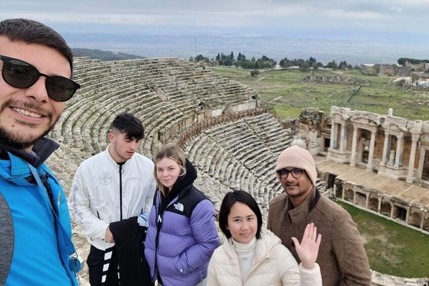 A group of people standing in front of an ancient amphitheater with ruins and columns. 3