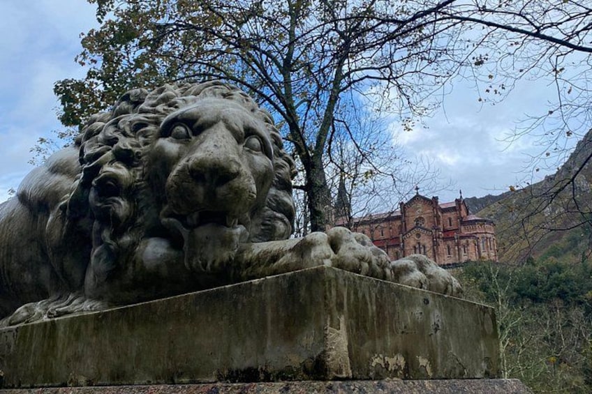 A stone lion statue, a building in the background, and a tree with bare branches. 1