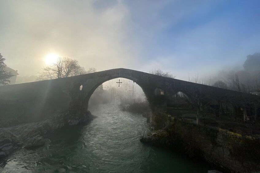 A stone bridge over a river with mist and a cross in the background. 4