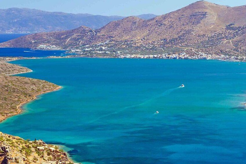 Un paisaje costero con mar azul cristalino, un pequeño bote y un pueblo lejano en la orilla. 1