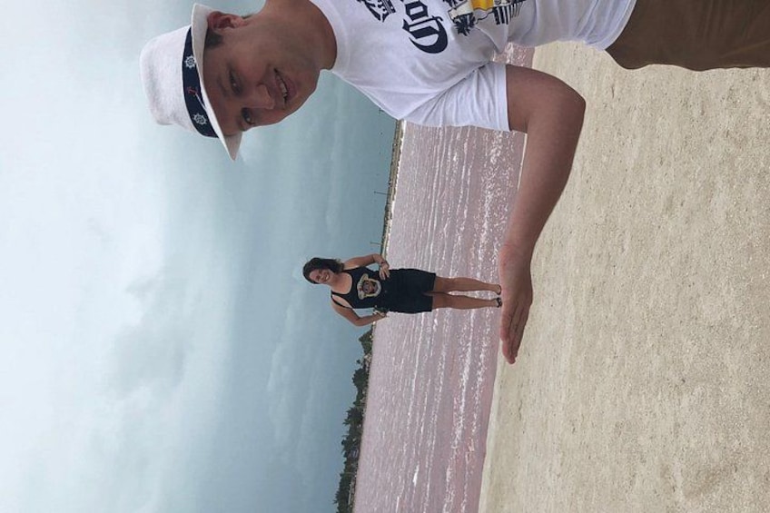 A person standing on a sandy beach with a body of water and greenery in the background. 2
