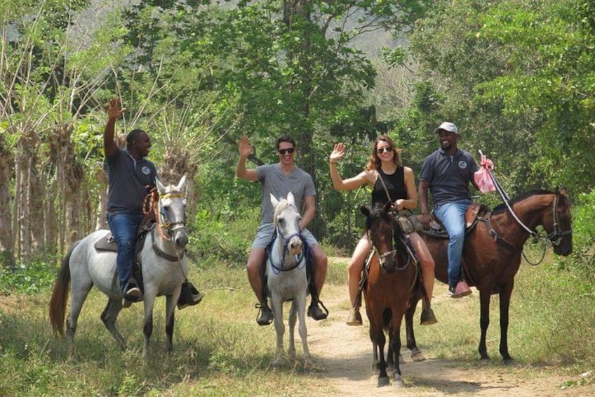 Cuatro personas montando a caballo por un sendero de tierra rodeado de vegetación. 1