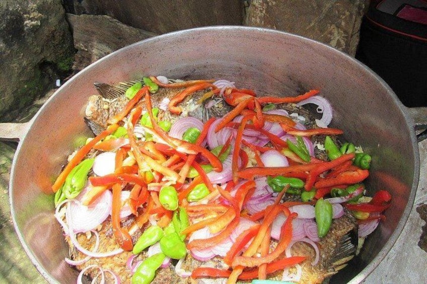 Un pescado entero con pimientos rojos y verdes en rodajas, cebollas y chiles verdes en una sartén. 3