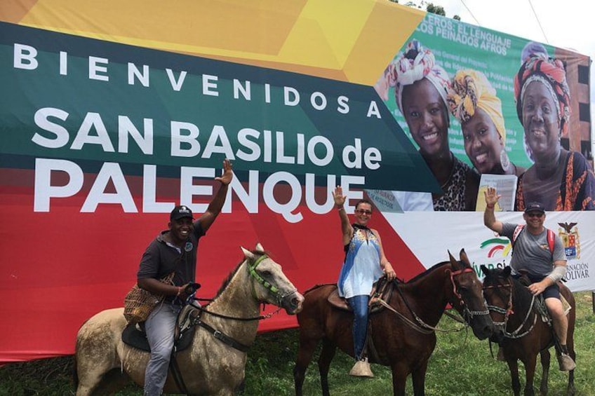 Tres personas a caballo frente a un gran cartel con texto. 4