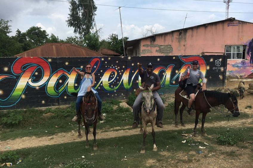 Tres personas montando caballos frente a un mural colorido. 5