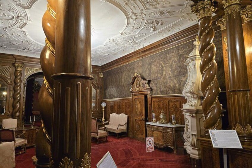 A grand room with ornate columns, a red carpet, and a large wooden cabinet. 5