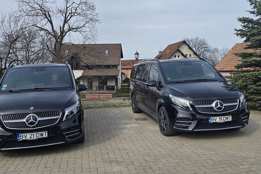 Two black Mercedes-Benz vehicles parked on a paved driveway in a residential area with houses and trees in the background. 2