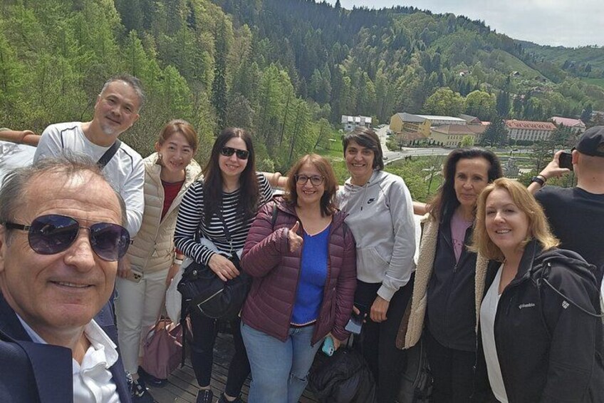 A group of people standing on a viewing platform with a mountainous landscape in the background. 2