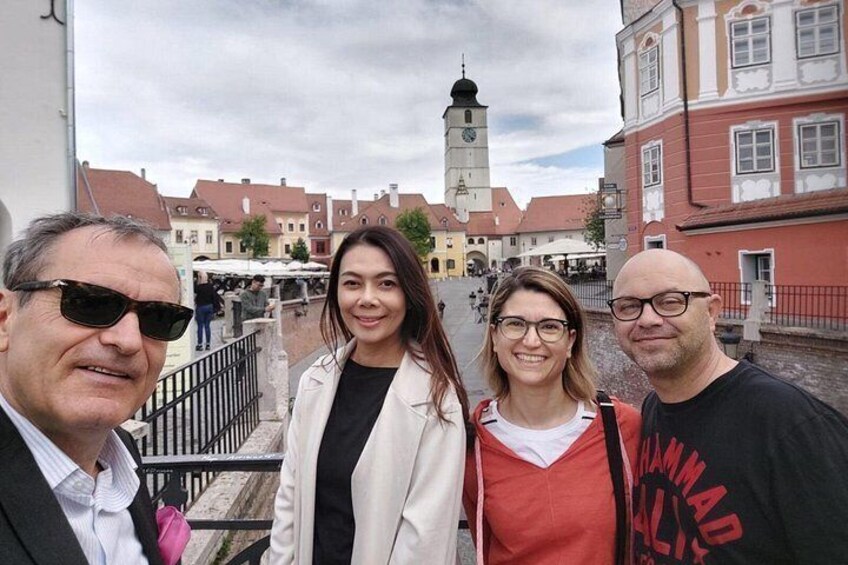 Un grupo de personas de pie en un entorno urbano al aire libre, con edificios históricos y una torre del reloj al fondo. 2