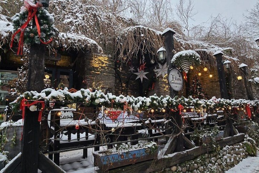 A snow-covered outdoor area with Christmas decorations, including garlands, lights, and a sign. 4