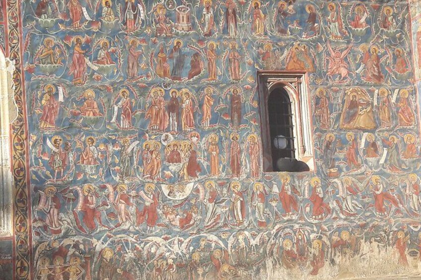 Een gedetailleerde muurschildering met religieuze figuren en een klein raam. 5