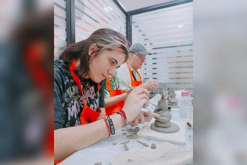 Dos personas trabajando la cerámica, con arcilla y herramientas de alfarería sobre la mesa. 3