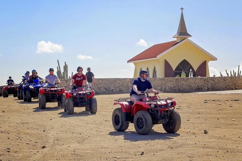 Menschen fahren mit Quads über hügeliges Sandterrain, im Hintergrund sieht man eine kleine Kirche. 4