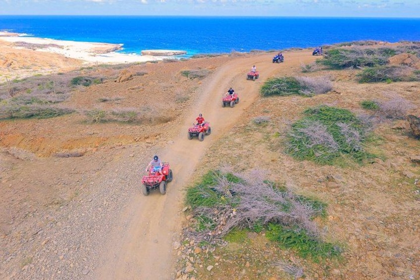 Un chemin de terre avec quatre véhicules tout-terrain, un paysage côtier avec l’océan en arrière-plan. 2