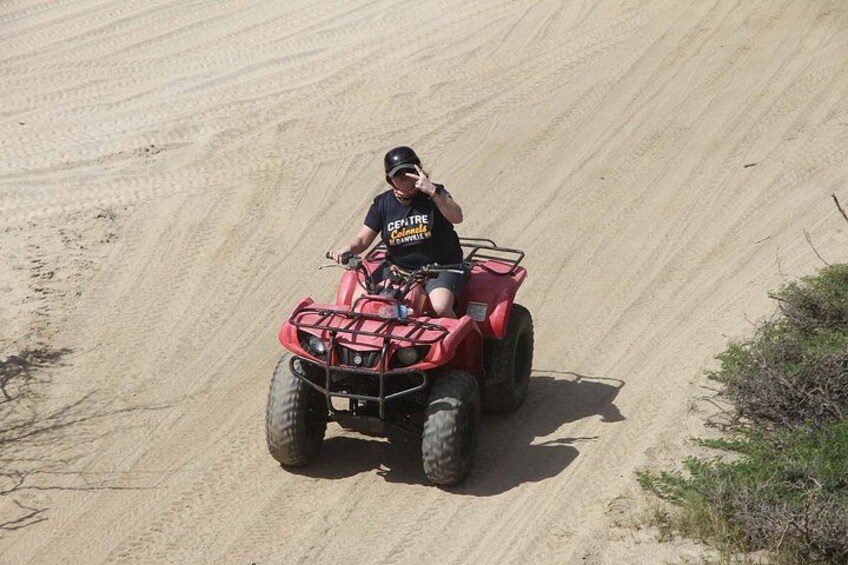 Eine Person fährt mit einem roten Quad über einen sandigen Hang. 3