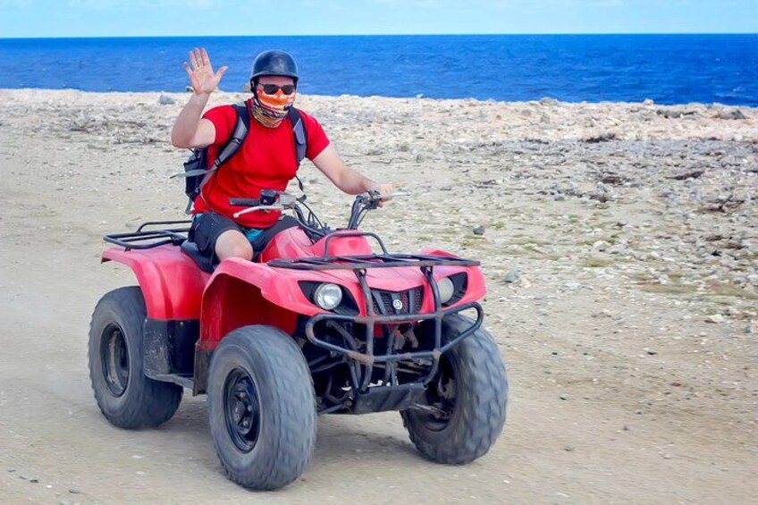Une personne conduit un quad rouge sur un chemin de terre près d’une côte rocheuse, avec l’océan en arrière-plan. 1