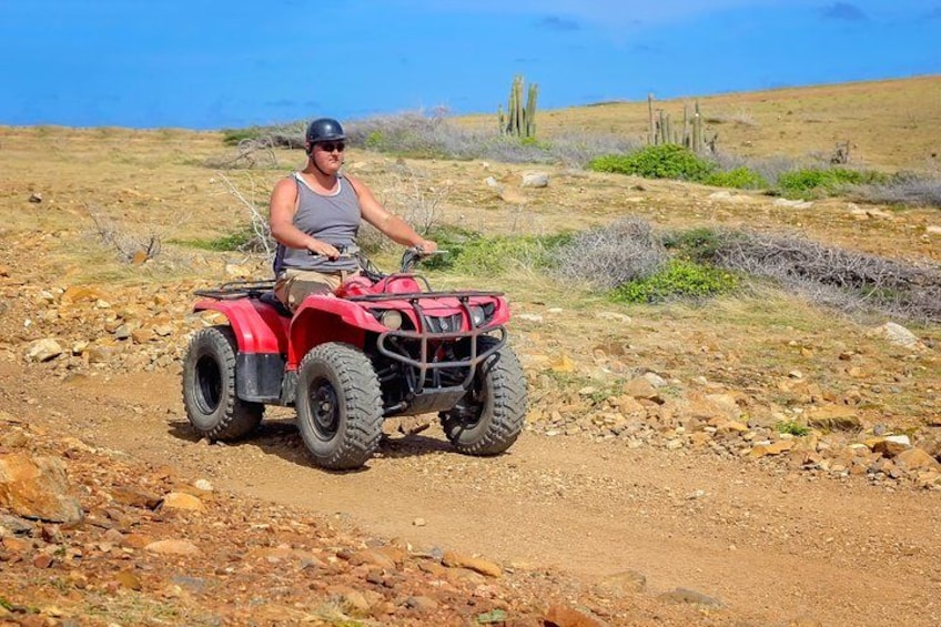 Une personne conduit un quad rouge sur un chemin de terre dans un paysage aride et rocheux, où la végétation est rare et le ciel est dégagé. 3