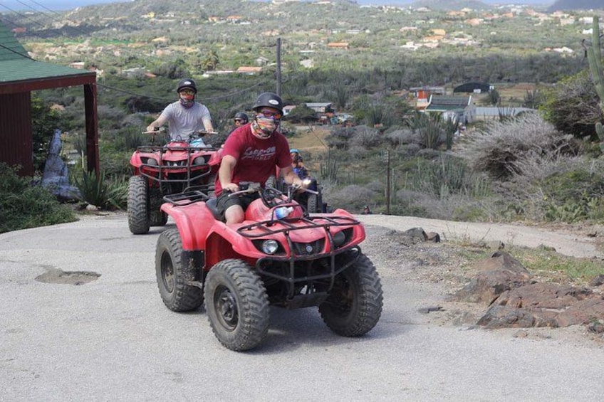 Two people riding red ATVs on a paved road with a rural landscape in the background. 4
