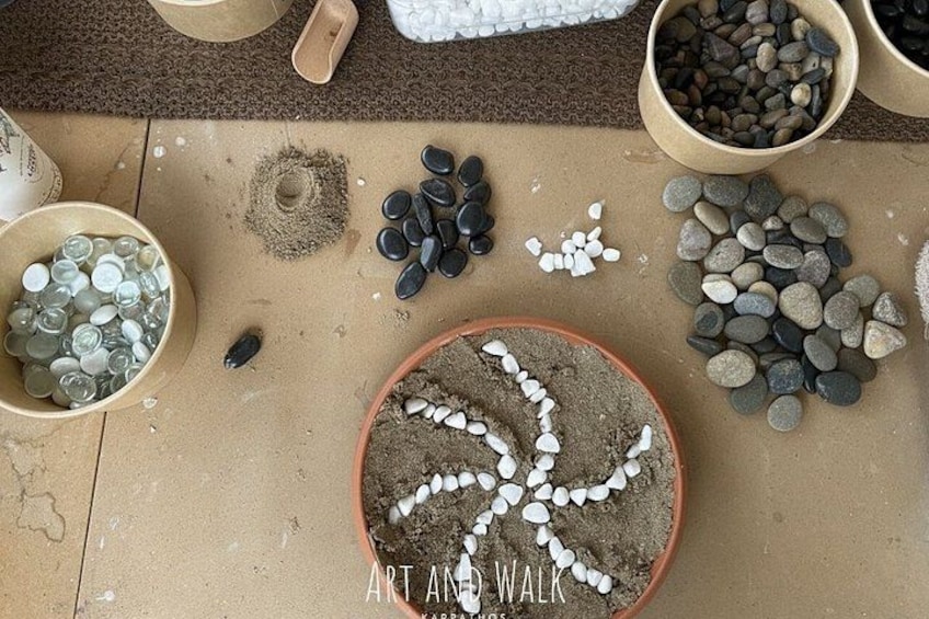 A collection of stones and pebbles arranged on a sandy surface, with a bowl of white pebbles in the center. 3