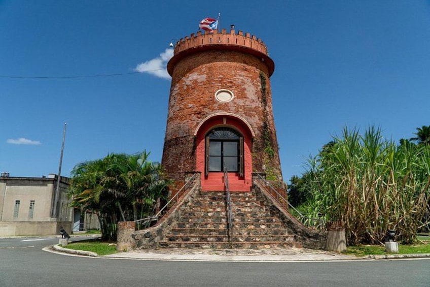 A brick tower with a red door and steps leading up to it, surrounded by palm trees and a clear sky. 3