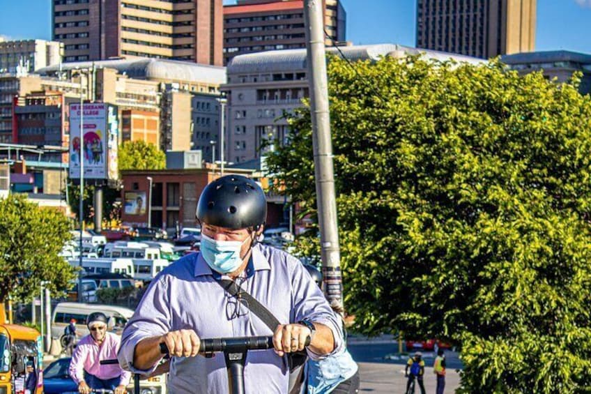 A person riding a scooter in an urban setting with buildings and trees in the background. 4
