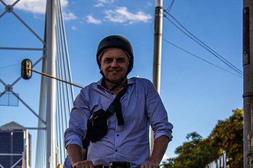 A person wearing a helmet and a checkered shirt standing in front of a bridge with cables. 3