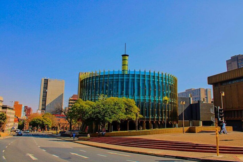 A modern building with a cylindrical shape and a spire, surrounded by trees and a clear blue sky. 2