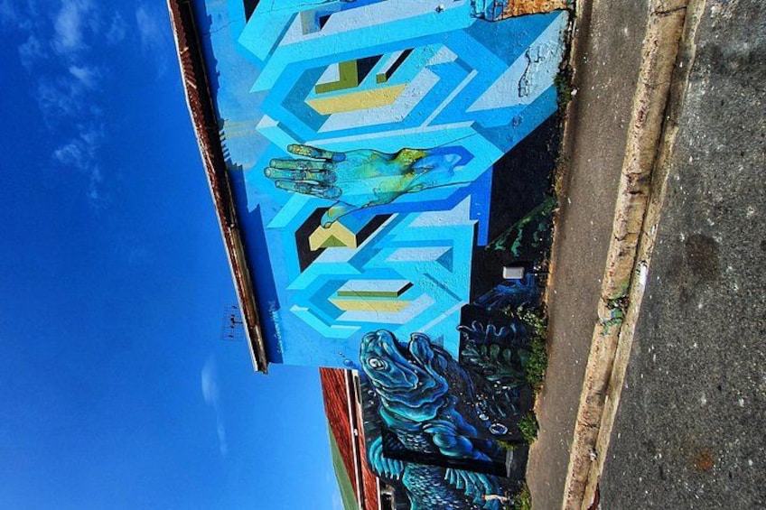 A blue geometric mural with a stylized figure, a road, and a building in the background. 1