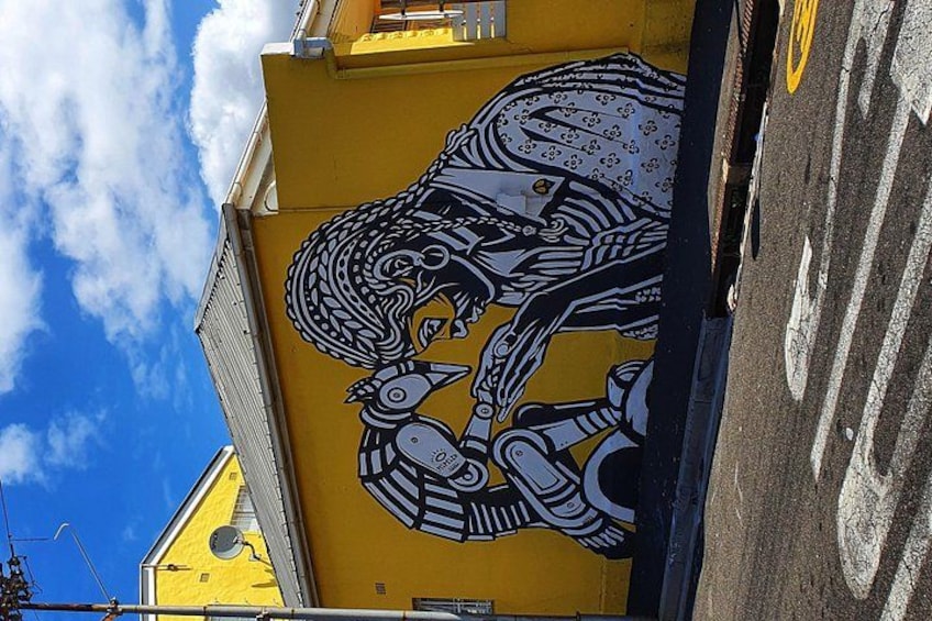 A yellow building with a mural of a bird and a mechanical bird. 4