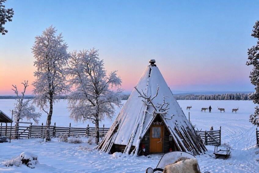Une cabane en bois recouverte de neige, avec un toit conique, entourée d’une clôture en bois et d’arbres également recouverts de neige. 4