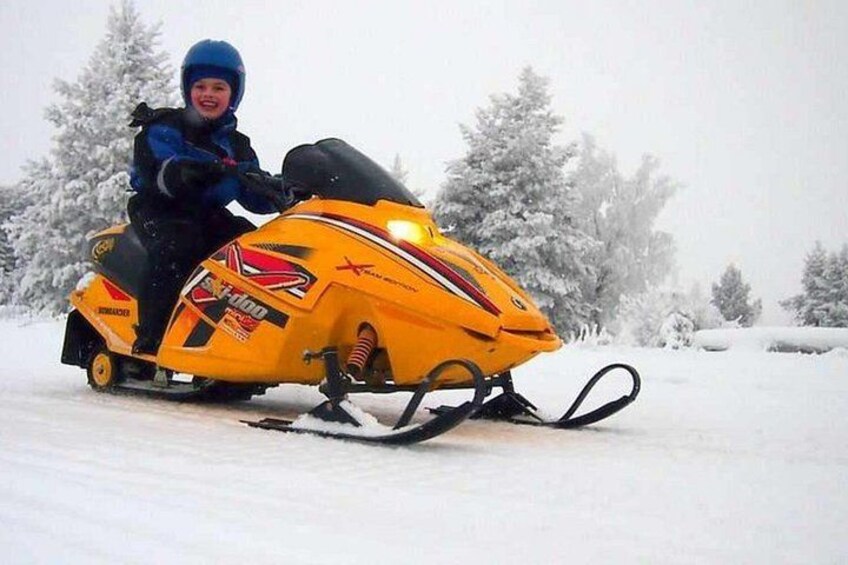 A person on a yellow snowmobile with a black seat and a blue helmet, surrounded by snow-covered trees. 3