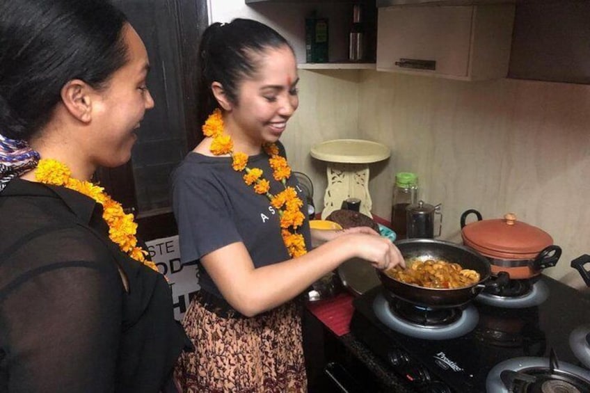 Deux femmes préparent un repas dans une cuisine, et elles portent des guirlandes de fleurs. 1