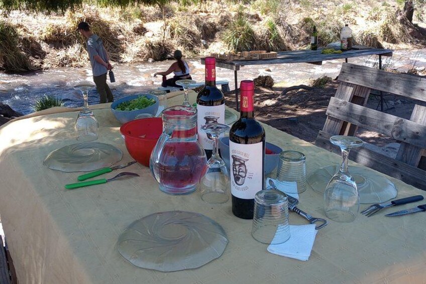 Een picknicktafel met wijnflessen, glazen en een rode schaal. 4