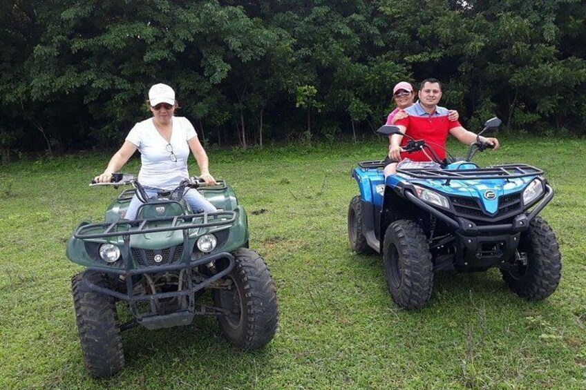 Two people on ATVs in a grassy field with trees in the background. 5